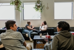 people sitting in a room on gray couches, talking to each other